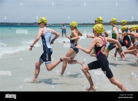 Group Of Female Athletes Race Into Surf From A Beach Start Of A