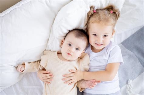 Premium Photo Two Sisters Children Cuddle On The Bed At Home The