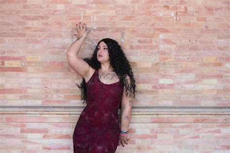 Beautiful Fat Lesbian Woman With Long Brown Curly Hair Dressed In Elegant Dress Leans Against A