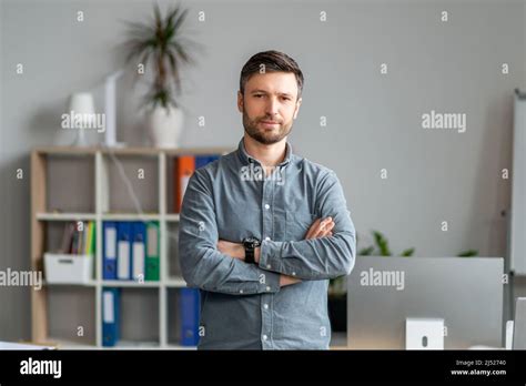 Portrait Of Mature Businessman Standing Near Workplace In Office