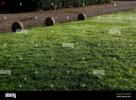 Green Lawn With Three Ornamental Stone Orbs Behind With Path Beyond