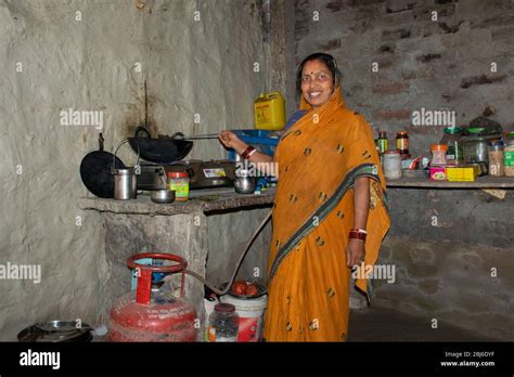 Happy Rural Woman Standing In Kitchen Cooking Food On Gas Stove India