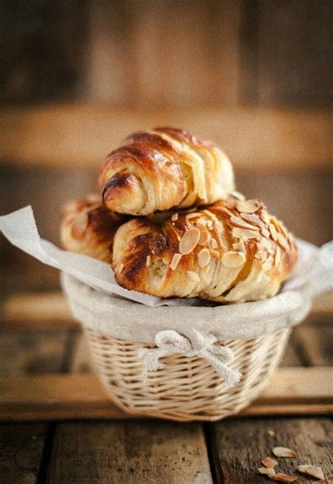 Three Croissants Sitting In A Basket On Top Of A Wooden Table