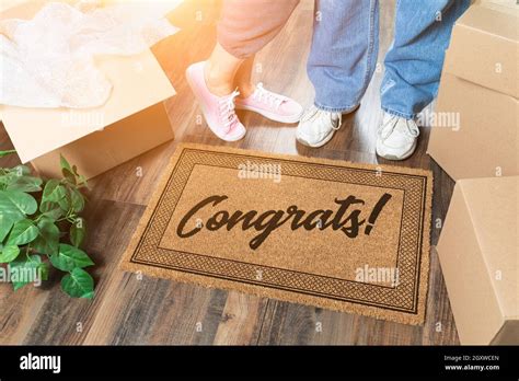 Man And Woman Unpacking Near Welcome Mat With Congrats Moving Boxes