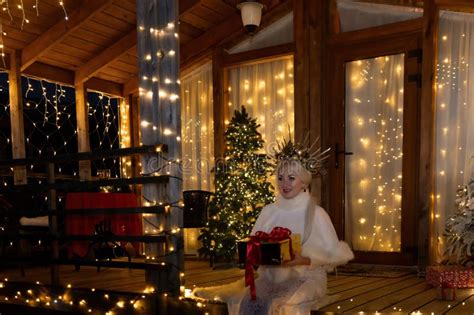 Happy Blonde As Snow Maiden In White Costume Wooden House Exterior Festive Setting Stock Photo