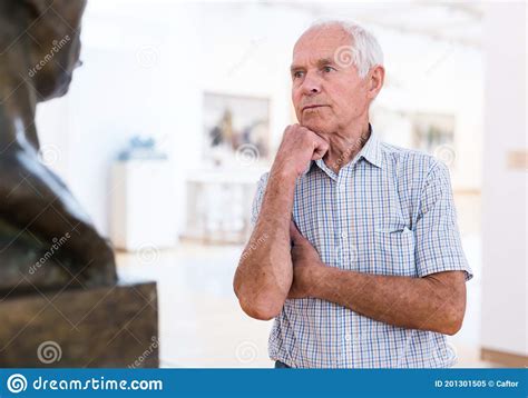 Mature European Man Examines Sculpture In An Exhibition In Hall Of An