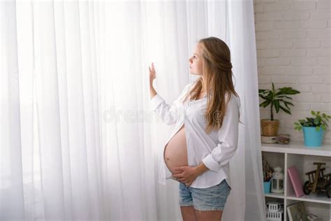 Side View Portrait Of A Young Pregnant Woman Stands And Looks Out The Window Stock Image