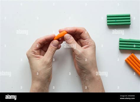 Woman Hands Making Small Carrot Polymer Clay On The White Background