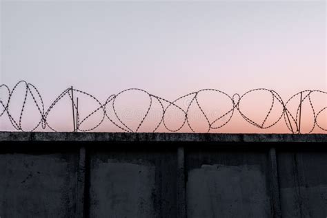 Concrete Wall With Barbed Wire Against A Blue Orange Evening Sky Stock