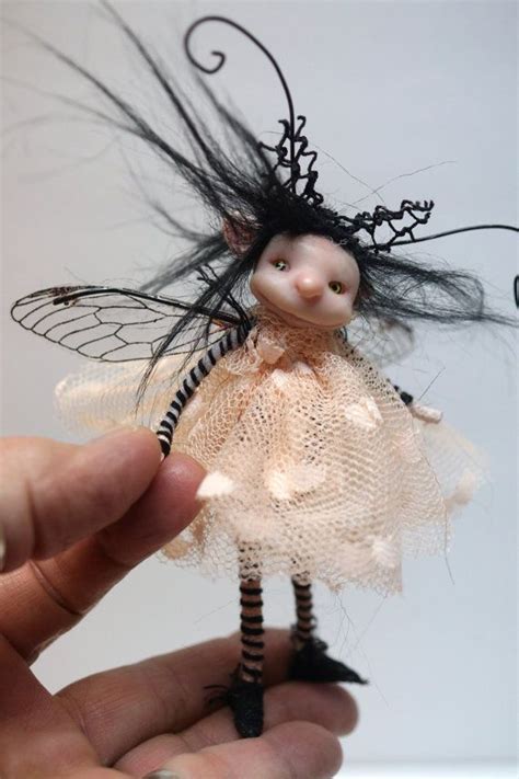 A Hand Holding A Small Doll With Black Hair And White Dress On It S Body