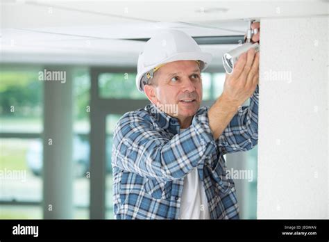 Mature Male Technician On Stepladder Fitting Cctv Camera Stock Photo