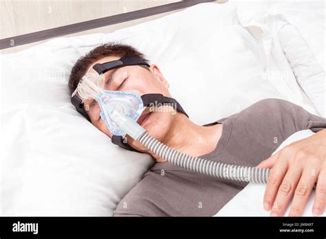 Middle Age Asian Man Sleeping In His Bed Wearing Cpap Headgear Mask Connected To Air Hose