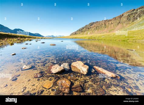 Sun Shines On The Rocky Peaks Reflected In The Clear Water Of Lake