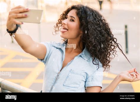 Portrait Of Happy Curly Brunette Woman Taking A Selfie While Showing