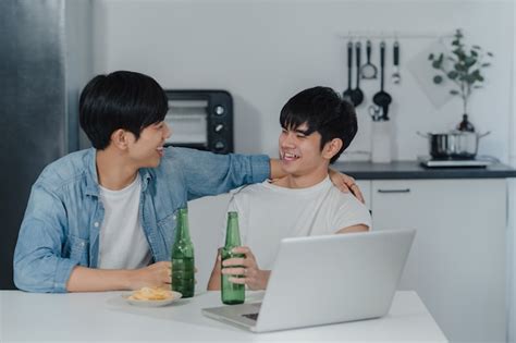 Jeune couple gay boit de la bière tout en utilisant un ordinateur portable à la maison moderne