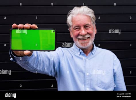 Old And Mature Man Holding His Smartphone Showing It At The Camera With