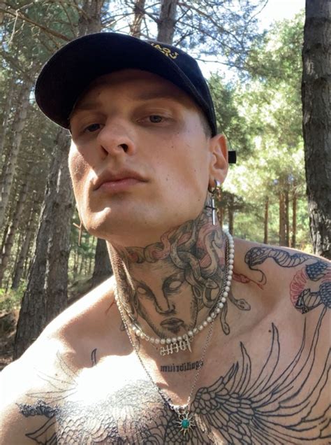 A Man With Tattoos On His Chest Standing In The Woods