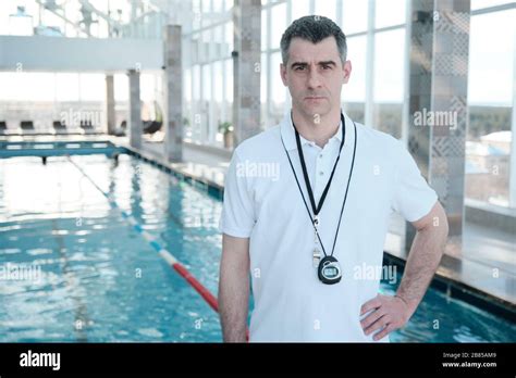 Portrait Of Serious Handsome Mature Swimming Coach In White Polo Shirt Standing At Pool Stock