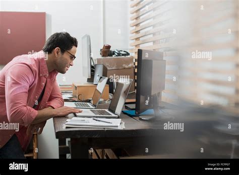 A Man In A Home Office With A Desk With Two Laptops Checking