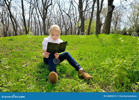 Assento E Leitura Da Menina Um Livro Na Natureza Imagem De Stock