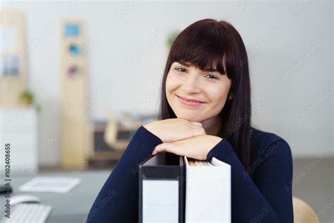 frau im büro stützt ihr kinn auf aktenordner Stock Foto Adobe Stock