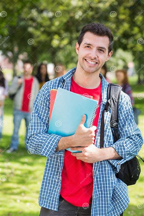 College Boy Holding Books With Blurred Students In Park Stock Image