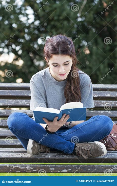 Smiling Young Woman Sitting On Bench And Reading Book Outdoor Stock