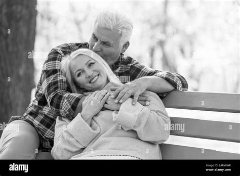 Black And White Portrait Of Loving Mature Couple Sitting On Bench In