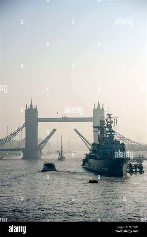 A Sailboat Passes Beneath Tower Bridge With Bascules Raised And Hms