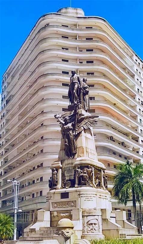 A Statue In Front Of A Tall Building With Balconies On The Top Floor