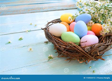 Colorful Easter Eggs In Nest With Flowers On Blue Wooden Background