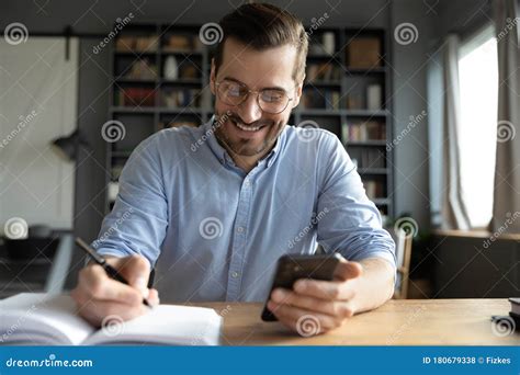 Smiling Businessman Wearing Glasses Using Phone Writing In Notebook