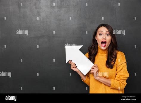 Shocked Brunette Woman In Sweater Pointing With Paper Arrow Away And