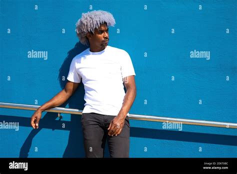 Black Man With Afro Hair Dressed In White Leaning Against A Blue Wall