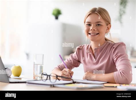 Smiling European Adolescent Girl Blonde Pupil Study At Home At Table With Laptop In Light