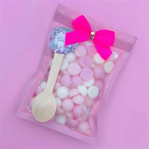 A Plastic Bag Filled With Pink And White Candies Next To A Wooden Spoon