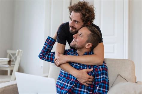 Encantadora pareja gay riendo juntos mientras están sentados en su sala