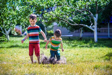 小男孩和他的兄弟在夏日公园玩耍穿着五颜六色衣服的孩子们在花园里的水坑和泥浆里跳来去孩子们在淋浴后在夏天的水坑里散步任何天气高清图片下载 正版