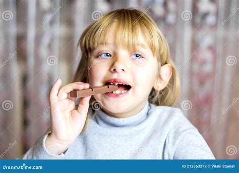 The Little Blonde Is Eating Chocolate Portrait Of A Girl Biting A Bar