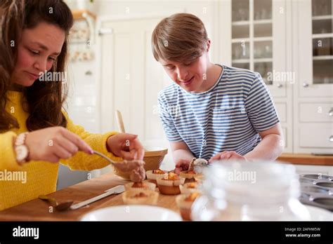 Young Downs Syndrome Couple Decorating Homemade Cupcakes With Icing In