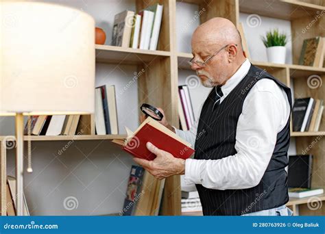 Mature Man Reading A Book While Standing In Living Room Stock Photo