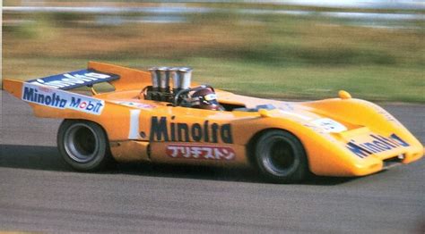 A Yellow Race Car Driving On A Track With Grass In The Backgrouund