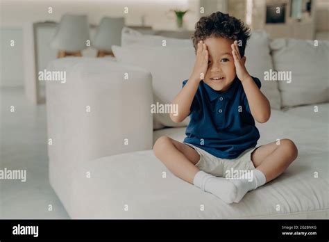 Cute Little Boy With Curly Hair Enjoying Game Of Hide And Seek At Home