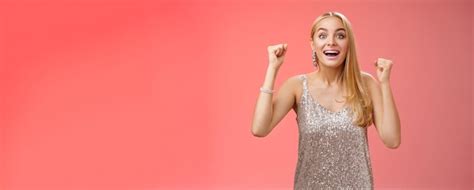 Überrascht fröhlich feiernde blonde junge Frau in silbernem trendigem Kleid Hände