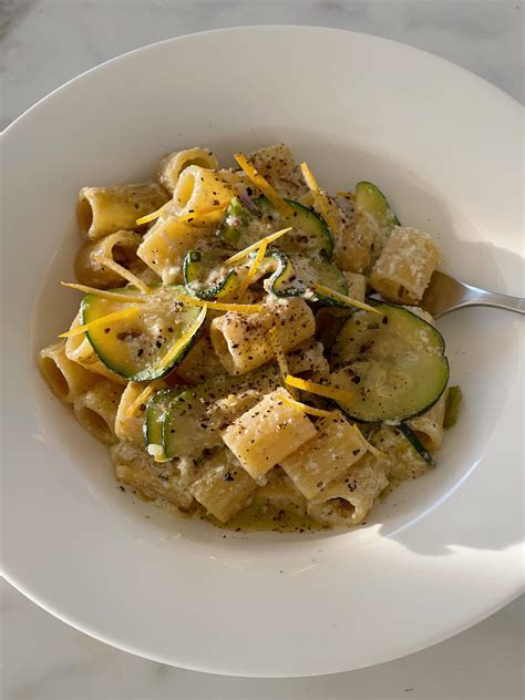 A White Plate Topped With Pasta Covered In Cheese And Cucumber Slices