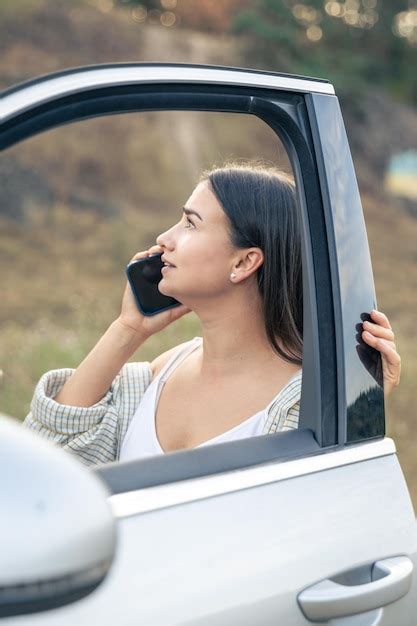 Mulher atraente falando ao telefone em pé ao lado do carro na natureza