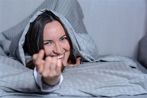 An Attractive Smiling Woman Lying In Bed Under A Blanket Looking At