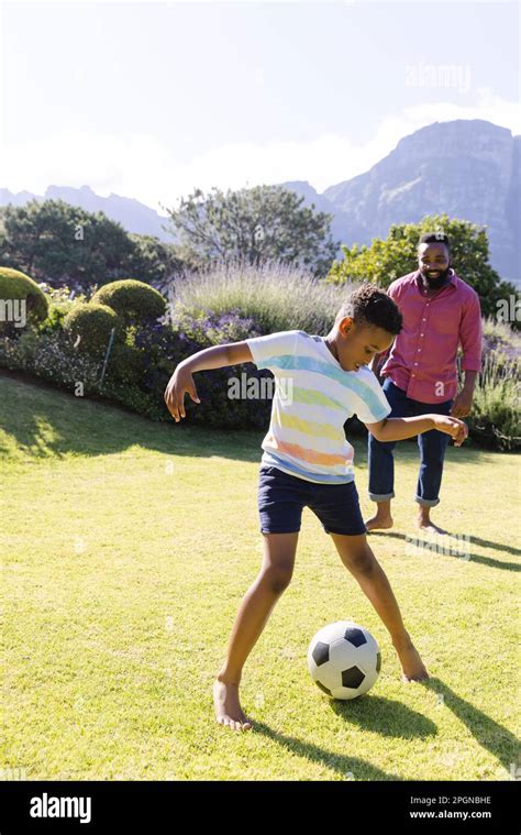 Happy African American Father And Son Playing Football In Garden