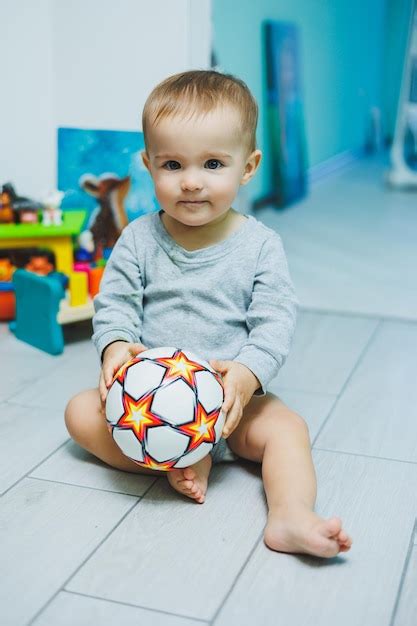 Um garotinho loiro está sentado no chão em uma sala os calcanhares