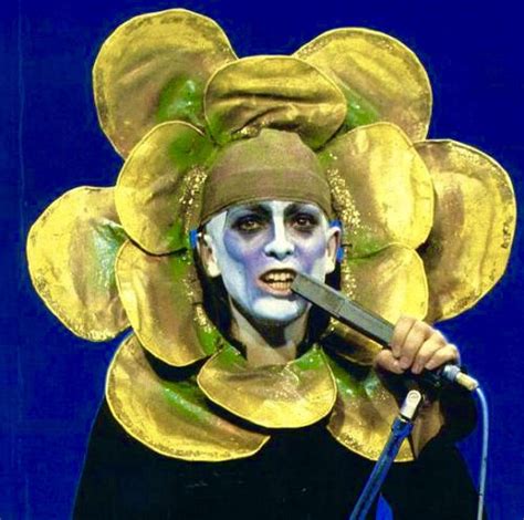 a man with painted face and yellow flowers on his head holding a microphone in front of him